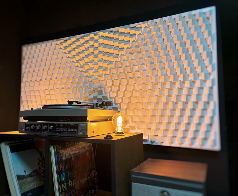 May include: A home audio setup featuring a turntable, amplifier, and a decorative wall panel. The wall panel has a repeating pattern of white, square blocks. A vintage-style light bulb sits on a small table next to the audio equipment.