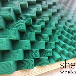 May include: A green wood wall art piece made of stacked wooden blocks. The blocks are arranged in a geometric pattern and are painted a vibrant green color. The piece is framed in natural wood and has the text "shepit WORKSHOP" at the bottom.