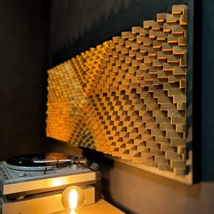 May include: A large, rectangular wooden wall art piece with a geometric, textured design. The artwork is made of small, square wooden blocks arranged in a stepped pattern. The piece is mounted on a dark frame. A turntable and a light bulb are in the foreground.