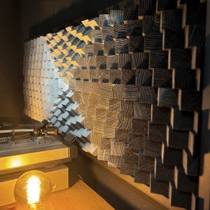 Puede incluir: Panel acústico de madera con un diseño degradado de bloques blancos a negros. Un tocadiscos y una bombilla Edison encendida en primer plano sugieren un ambiente musical. El panel está diseñado para la absorción del sonido.