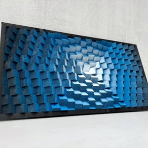 May include: A blue and black abstract wall art piece made of wood. The wood is arranged in a pattern of squares that create a 3D effect. The squares are painted in shades of blue, from light blue to dark blue.