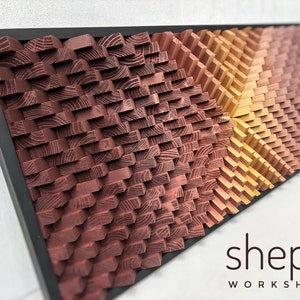 以下が含まれることがあります： 幾何学模様の木材で作られた額縁付きの壁掛けアート作品。木材は赤、オレンジ、黄色の色合いで染色されています。作品名は「shepit workshop」です。