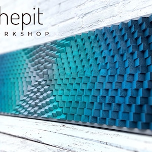 May include: A wall art piece made of wood with a gradient of blue and teal colours. The wood is arranged in a pattern of squares, creating a textured surface. The piece is titled "shepit WORKSHOP".