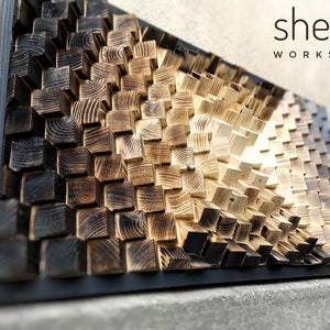 May include: A wall art piece made of wood blocks, with a gradient of colors from black to light brown. The blocks are arranged in a geometric pattern, creating a 3D effect. The piece is signed "shepit WORKSHOP" in the top right corner.
