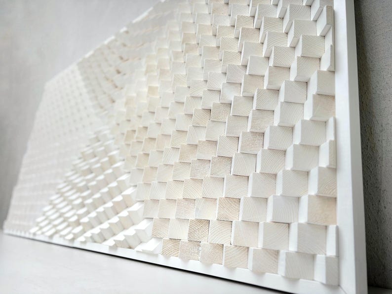 May include: White wooden wall art with a geometric design. The artwork features a series of small, square wooden blocks arranged in a pattern that creates a textured, three-dimensional effect. The blocks are painted white and mounted on a white frame.