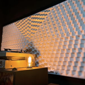 May include: A light-filled room with a vintage turntable, a decorative light bulb, and a large, textured wall panel. The wall panel is made of small, square, white blocks arranged in a repeating pattern. The scene evokes a retro aesthetic.