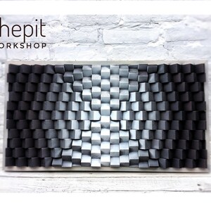May include: A black and white 3D wall art piece made of wood cubes. The cubes are arranged in a gradient pattern, with the darkest cubes on the left and the lightest cubes on the right. The piece is mounted on a white wall.