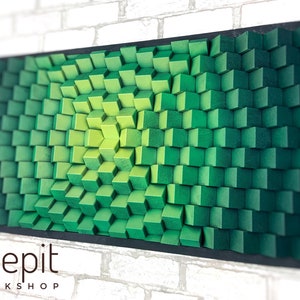 May include: A green and yellow 3D wall art piece made of wood blocks. The blocks are arranged in a wave pattern, creating a sense of depth and movement. The piece is framed in black and has the text "shepit workshop" at the bottom.