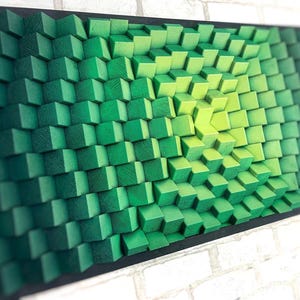 Może przedstawiać: Abstrakcyjny obraz ścienny w kolorze zielonym i żółtym wykonany z drewnianych kostek. Kostki są ułożone w wzór, który tworzy efekt 3D. Obraz jest oprawiony w czarną ramę.