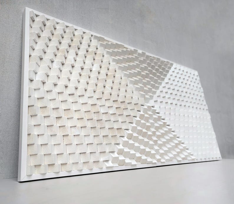 May include: A white, geometric wooden wall art piece. The artwork features a repeating pattern of small, square blocks arranged in a textured, three-dimensional design. The blocks are painted white and mounted on a white frame.