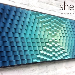 May include: A wall art piece made of wood blocks in shades of blue and green, arranged in a geometric pattern. The blocks are stacked in a way that creates a 3D effect. The piece is framed in black and has the text "shepit WORKSHOP" in the top right corner.