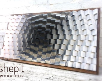 May include: A 3D wall art piece made of wood with a geometric pattern of cubes. The cubes are painted in shades of gray and white, creating a gradient effect. The piece is framed in a dark wood frame. The text "shepit WORKSHOP" is visible at the bottom of the image.