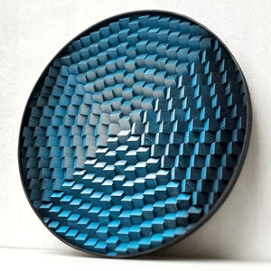 Może przedstawiać: Okrągła dekoracja ścienna wykonana z drewna z niebiesko-białym geometrycznym wzorem. Wzór składa się z małych kwadratów ułożonych w okrągły wzór.