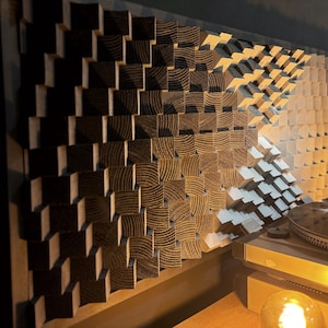May include: Wooden acoustic panel with a geometric design, constructed from blocks that shift from dark brown to light wood. A record player is partially visible, indicating a product related to music or audio.