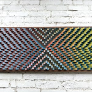May include: A rectangular wall art piece composed of numerous small, vertical wooden blocks arranged in a geometric pattern. The blocks are painted in gradients of blue, red, orange, and yellow, creating a textured, three-dimensional surface.