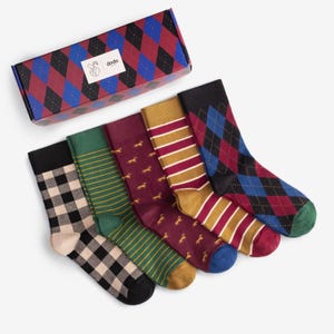 May include: A set of five colorful socks with various patterns, including plaid, stripes, and argyle. The socks are in a variety of colors, such as black, green, burgundy, and gold. The socks are displayed next to a patterned box with the brand name "dodo".