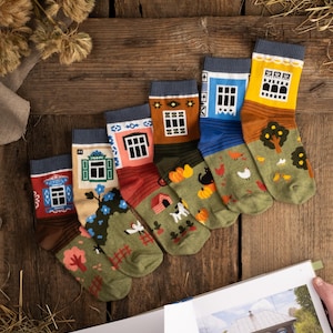 Peut inclure: Un ensemble de huit chaussettes colorées avec un motif fantaisiste de maisons aux fenêtres et aux portes détaillées. Chaque chaussette a un fond vert avec diverses illustrations d'animaux, de plantes et d'autres détails.