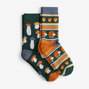 May include: Two pairs of socks with nature-themed patterns. One pair features white and orange mushrooms on a dark green background. The other pair has orange and yellow stripes, acorns, and hedgehogs on a dark green background.