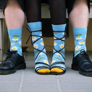 Può includere: Calzini azzurri con motivo a margherite, abbinati a scarpe nere. Una persona indossa i calzini con lacci neri legati alle caviglie. L'altra persona indossa scarpe nere.