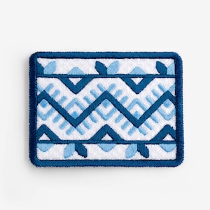 May include: Rectangular white coaster with a blue embroidered geometric pattern. The design features a series of zigzags and leaf-like shapes in varying shades of blue. The coaster has a dark blue border.