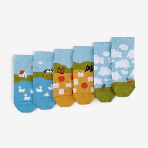 May include: Six pairs of socks with various landscape designs. Each sock features a different scene: ducks on a lake, a cow in a field, a dog with apples, a black cat, clouds, and a fox. The socks have blue, green, yellow, and white colors.