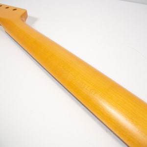 May include: A natural wood guitar neck with a light brown finish. The neck has six tuning pegs and a fretboard.
