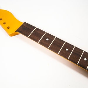 May include: A yellow guitar neck with a brown rosewood fretboard and white dot inlays.
