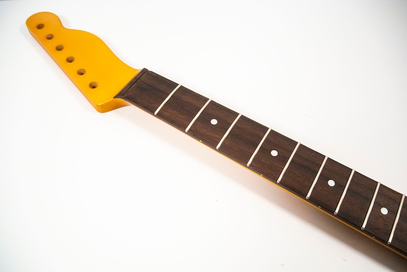 May include: A yellow guitar neck with a brown rosewood fretboard and white dot inlays.
