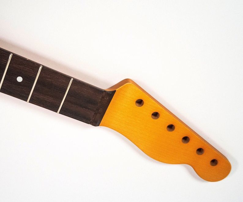 May include: A close-up of a guitar neck with a dark wood fretboard and a light wood headstock with six tuning pegs.