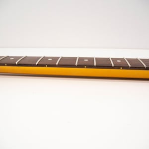 May include: Close-up of a brown guitar neck with white dot inlays and silver frets. The neck is attached to a yellow body.