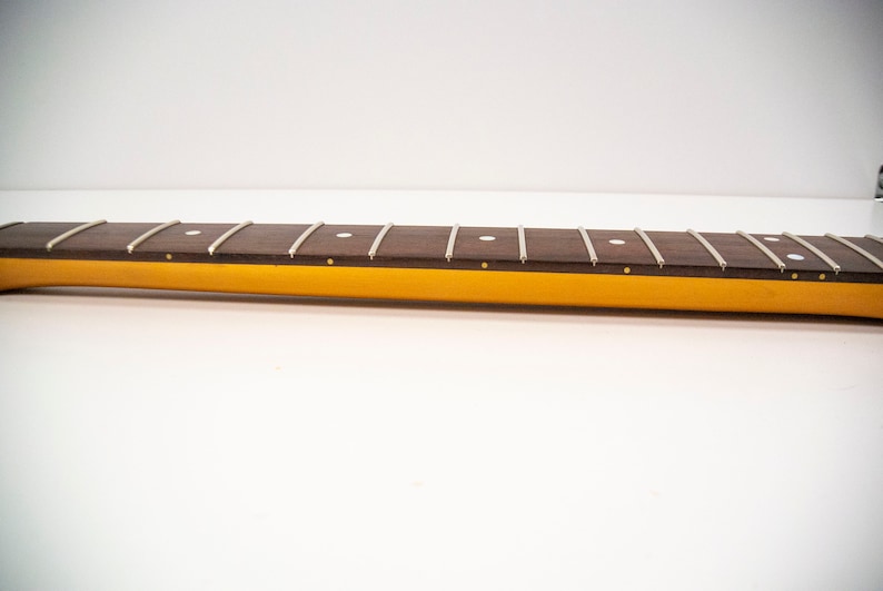 May include: Close-up of a brown guitar neck with white dot inlays and silver frets. The neck is attached to a yellow body.
