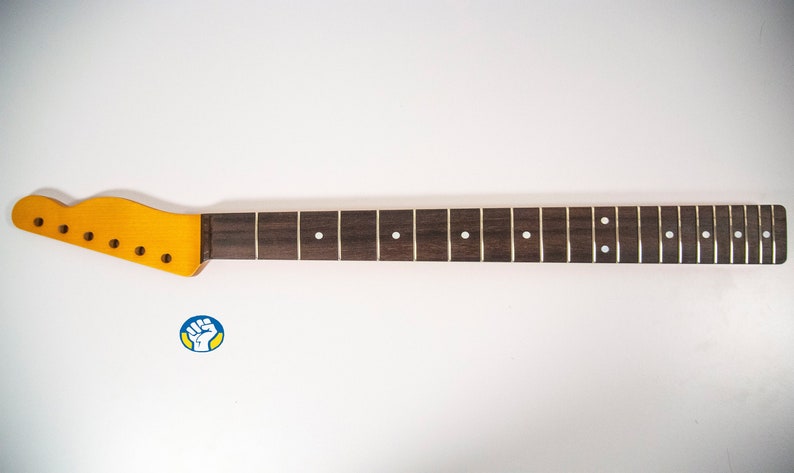 May include: A dark brown guitar neck with a light brown headstock and white dot inlays. The neck is made of rosewood and has 22 frets.