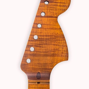 Könnte beinhalten: Nahaufnahme eines Gitarrenkopfes mit natürlicher Holzlackierung. Der Kopf ist aus Ahornholz gefertigt und hat eine charakteristische Form. Die Stimmmechaniken sind auf dem Bild nicht zu sehen.