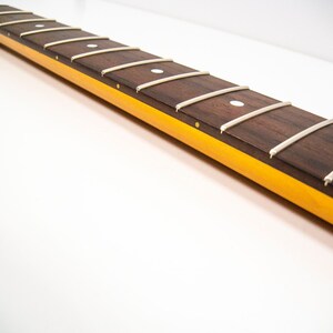 May include: A close-up of a guitar neck with a rosewood fretboard and white dot inlays. The neck is finished in a yellow color.