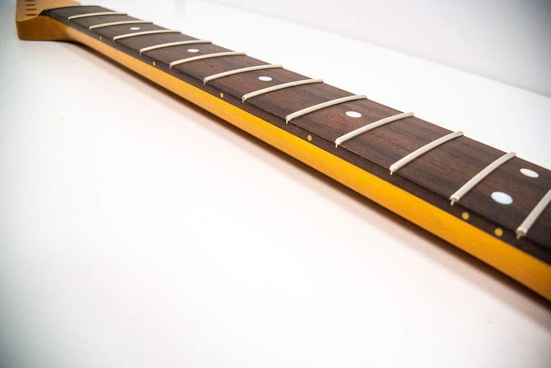 May include: A close-up of a guitar neck with a rosewood fretboard and white dot inlays. The neck is finished in a yellow color.