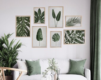 May include: A collection of seven framed botanical prints featuring various green tropical leaves. The prints are displayed on a white wall above a white sofa with green pillows. The frames are light wood, and the overall aesthetic is modern and natural.