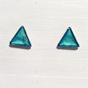 May include: A pair of teal triangle stud earrings with a silver-colored border. The earrings have a metallic, iridescent finish, and are set against a white background.