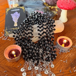 May include: A collection of black beaded necklaces featuring faceted glass beads strung on silver-toned metal chains. Each necklace ends with a silver-toned metal extender chain and a small circular charm engraved with a delicate floral design.