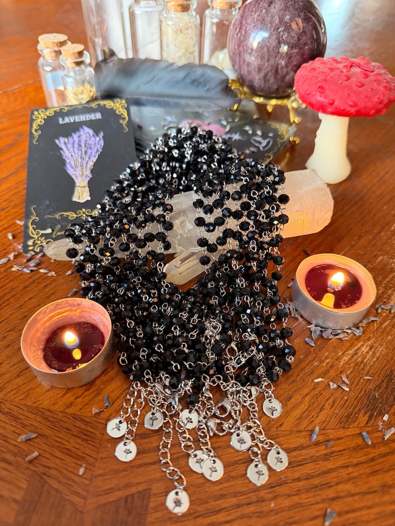 May include: A collection of black beaded necklaces featuring faceted glass beads strung on silver-toned metal chains. Each necklace ends with a silver-toned metal extender chain and a small circular charm engraved with a delicate floral design.