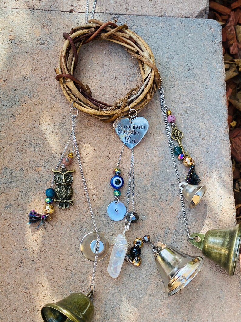 May include: A handcrafted wind chime featuring a woven twig wreath. Decorative elements include a metal heart with the text "Do no harm but take no shit", an owl charm, beads, a key charm, and brass bells.