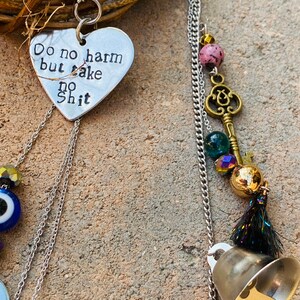 May include: A handmade wind chime with a heart-shaped pendant that reads "Do no harm but take no shit." The chime features a silver chain, decorative beads, a brass key charm, and a small bell. The wind chime is attached to a woven wreath.