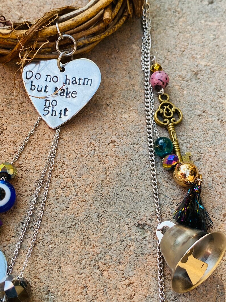 May include: A handmade wind chime with a heart-shaped pendant that reads "Do no harm but take no shit." The chime features a silver chain, decorative beads, a brass key charm, and a small bell. The wind chime is attached to a woven wreath.