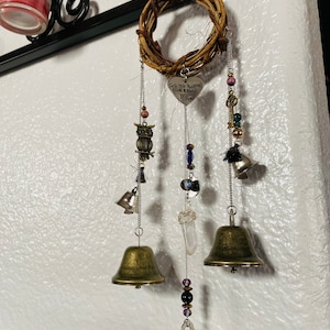 May include: A decorative wind chime featuring a woven wreath, metal bells, and various charms. The charms include an owl, beads, and a heart-shaped pendant with the text "Go no harm but take no shit". The bells are in varying sizes and finishes.