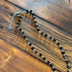 May include: A necklace featuring a series of faceted black beads linked by a silver-toned metal chain. The piece includes a silver-toned lobster claw clasp and an adjustable extender chain finished with a small, circular metal charm at the end.