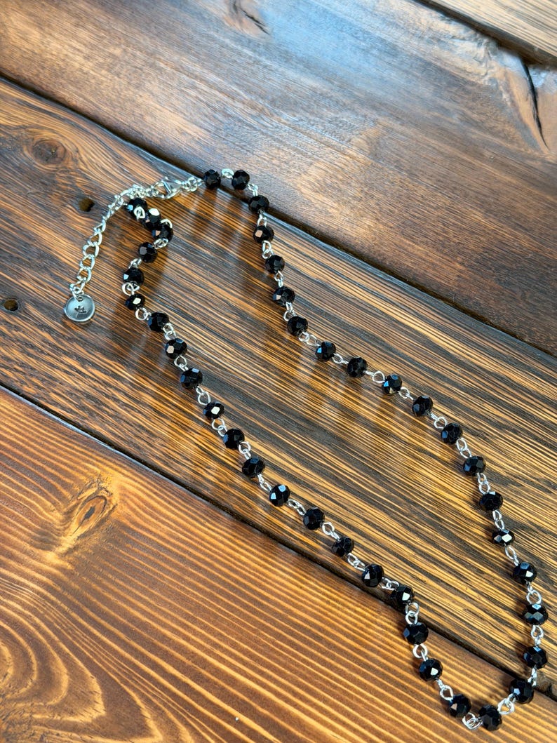 May include: A necklace featuring a series of faceted black beads linked by a silver-toned metal chain. The piece includes a silver-toned lobster claw clasp and an adjustable extender chain finished with a small, circular metal charm at the end.
