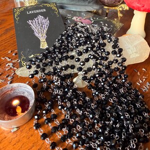 May include: A multi-strand necklace featuring faceted black beads linked together with silver-toned metal wire. The necklace is draped in several layers, creating a cascading effect of dark, reflective beads that catch the light.