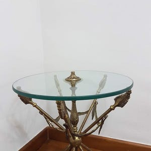 Può includere: Un tavolino rotondo con piano in vetro trasparente. Il tavolo ha una base in metallo color ottone con un design a freccia. Il tavolo misura circa 61 cm di diametro e 51 cm di altezza.