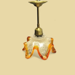 Op de afbeelding: Een gouden en heldere glazen hanglamp met een bloemvormige kap. De kap heeft een getextureerd, mat glazen oppervlak met oranje en bruine accenten.