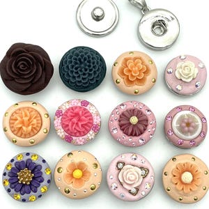 May include: Assortment of 12 snap buttons featuring various floral designs. The buttons are in shades of pink, peach, purple, brown, and green. Each button has a different floral design, including roses, daisies, and carnations. The buttons are perfect for adding a touch of elegance to any project.