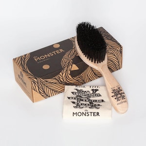 May include: A wooden hair brush with black bristles, a cardboard box labelled "the MONSTER by Kent Brushes," and a small white cloth featuring the text "Estd. 1777, C.B KENT & SONS LTD, BEST BRITISH BRUSHES, the MONSTER" printed in black ink.